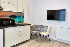 A compact kitchen with a microwave, toaster, and coffee maker. A flat-screen TV is mounted on the wall. The room has a small dining table with two chairs. - Apartamente La Butoaie (Navodari)