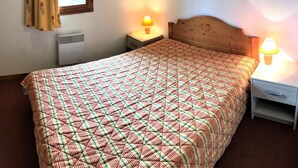Een eenpersoonsbed met een bedsprei met patroon, twee nachtkastjes met lampen, een raam met gordijnen en een wandradiator.
