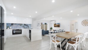 Una cocina moderna con armarios blancos, una isla central y un comedor con mesa de madera y sillas blancas.