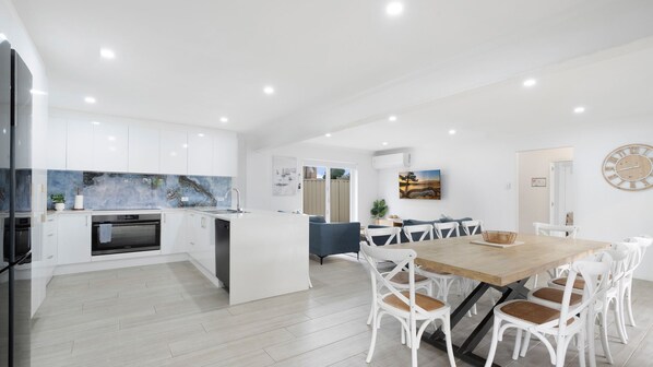 A modern kitchen with white cabinetry, a central island, and a dining area with a wooden table and white chairs.