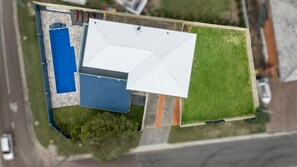 Vista aérea de una propiedad con un edificio blanco grande, una estructura azul y un césped verde.