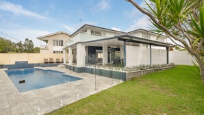 Una casa moderna con piscina, terraza cubierta y césped bien cuidado.