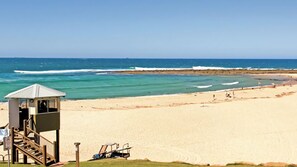 Une plage avec une tour de surveillance pour les sauveteurs, une eau d’un bleu limpide et un rivage sablonneux.