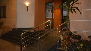 A staircase with metal railings leading to an upper floor, a wall-mounted light fixture, and a potted plant. - The Grand Neelam Hotel (Raipur)