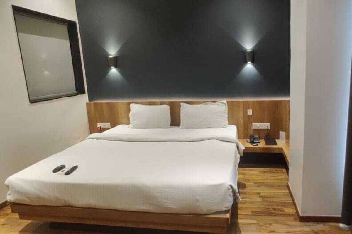 A hotel room with a bed, bedside tables, a wall-mounted light, and a curtain.