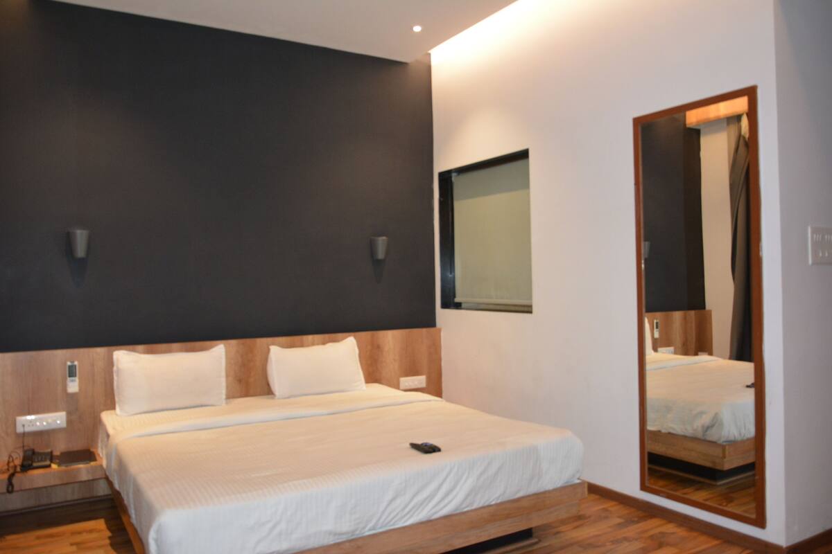 A modern hotel room with a large bed, a bedside table, a mirror, and a wall-mounted light fixture.