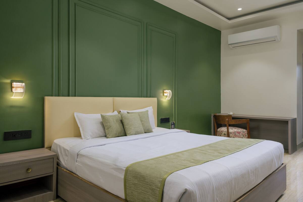 A neatly made bed with a green throw, a bedside table with a lamp, and a small desk with a chair.