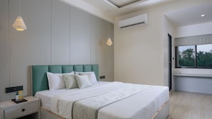 A modern bedroom with a large bed, a nightstand, a wall-mounted air conditioner, and a window with a view of greenery. - The Grand Neelam Hotel (Raipur)