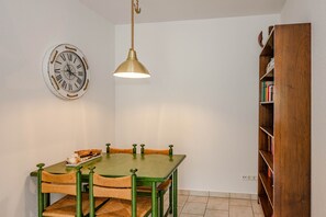 Un comedor con una mesa de madera, sillas, una lámpara colgante, un reloj de pared y una estantería.