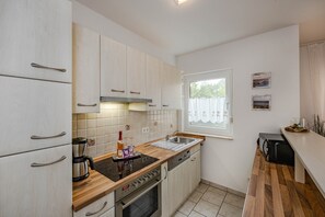 A modern kitchen with white cabinets, a wooden countertop, a built-in oven, and a window with a view. - Ferienappartement mit Terrasse, Strandkorb, Wlan und Pkw-stellplatz (Koserow)
