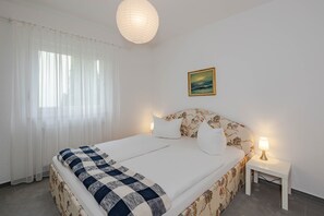 Una habitación de hotel con una cama, una mesita de noche, una lámpara, un cuadro y cortinas traslúcidas.