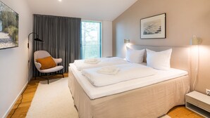 Ein modernes Schlafzimmer mit einem großen Bett, einem Sessel, einem Schreibtisch und einem Fenster mit Vorhängen.