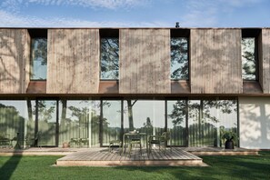 A modern building with large windows and a deck area with outdoor furniture.