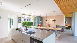 Eine moderne Küche mit einer großen Kochinsel, einem Essbereich mit Holztisch und Blick ins Freie.
