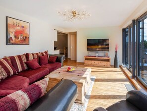 Un salon moderne avec un canapé rouge, une table basse en bois et un téléviseur posé sur un meuble en bois.
