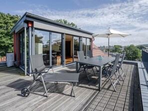 Une terrasse extérieure moderne avec un espace clos par des parois de verre, une table avec des chaises et un grand parasol.
