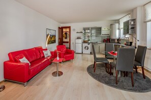 En moderne lejlighed med en rød lædersofa, et spiseområde med bord og stole, et køkken med hårde hvidevarer, og et lille vaskerum.