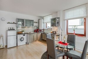 Una cocina moderna con electrodomésticos de acero inoxidable, un comedor con mesa de vidrio y vistas al exterior a través de una ventana.