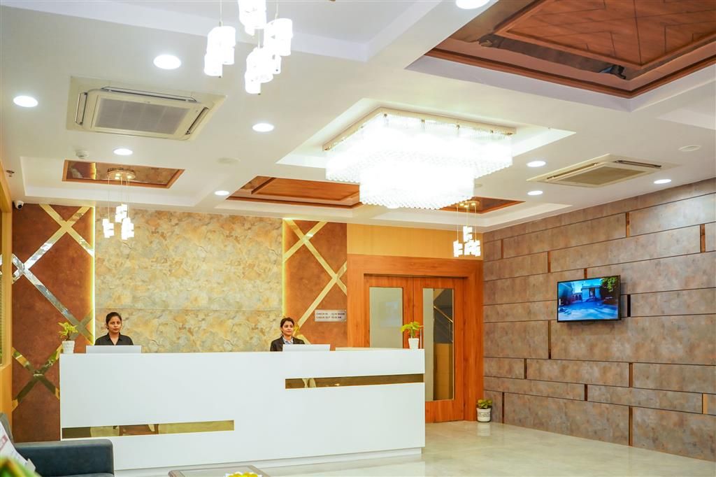 Zona de recepción de hotel con diseño moderno, que incluye un mostrador de recepción, una gran lámpara de araña, un televisor montado en la pared y una pared de piedra.