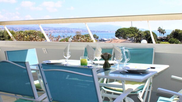 A dining area with a table set for two, overlooking a scenic view of the sea and a distant cityscape. - Beautiful 3-room apartment with terrace and parking in Villeneuve-Loubet Plage (Villeneuve-Loubet)