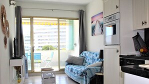 A modern apartment with a balcony, a sofa, a small table, and a kitchen area. - Beautiful 3-room apartment with terrace and parking in Villeneuve-Loubet Plage (Villeneuve-Loubet)