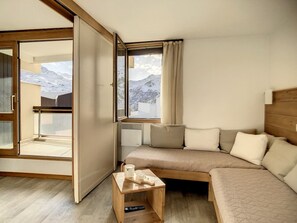 A modern room with a sofa, a small wooden table, and a sliding glass door leading to a balcony.
