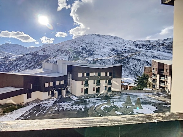 A modern building with a flat roof and multiple windows, surrounded by snow-covered mountains and a clear sky.