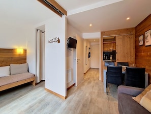 Una sala de estar moderna con un sofá, una zona de comedor con sillas y una cocina visible a través de una puerta abierta.