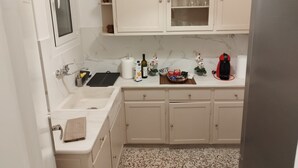 Una cocina compacta con armarios blancos, encimera de mármol y refrigerador de acero inoxidable.