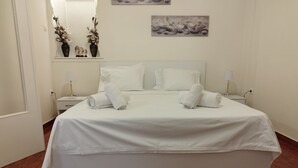 Una cama bien hecha con sábanas y toallas blancas, una mesita de noche con lámpara, y un cuadro colgado en la pared.