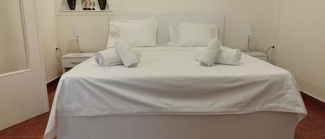 Una cama bien hecha con sábanas y toallas blancas, una mesita de noche con lámpara, y un cuadro colgado en la pared.