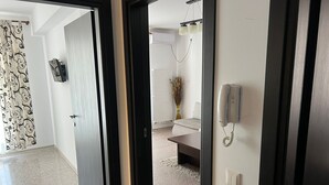 A hallway with a door leading to a room with a sofa and a vase of dried plants. - Apartamente Aquarium (Navodari)