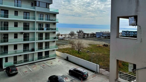 A multi-story building with balconies, a parking area with cars, and a view of the sea. - Apartamente Aquarium (Navodari)
