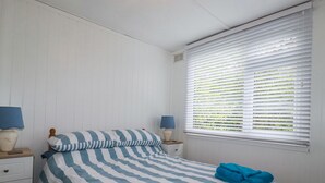 Un dormitorio con una colcha a rayas, dos mesitas de noche con lámparas, una ventana con persianas y una toalla azul sobre la cama.