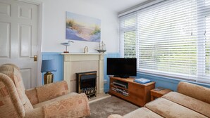 Una sala de estar con chimenea, televisor y un ventanal con persianas.
