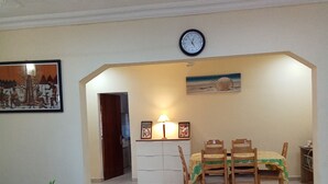 A dining area with a table and chairs, a clock on the wall, and a painting above the door.