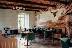 A restaurant with brick walls, a cow skull decoration, and green upholstered chairs. - Domaine des Lumières (Aisonville-et-Bernoville)