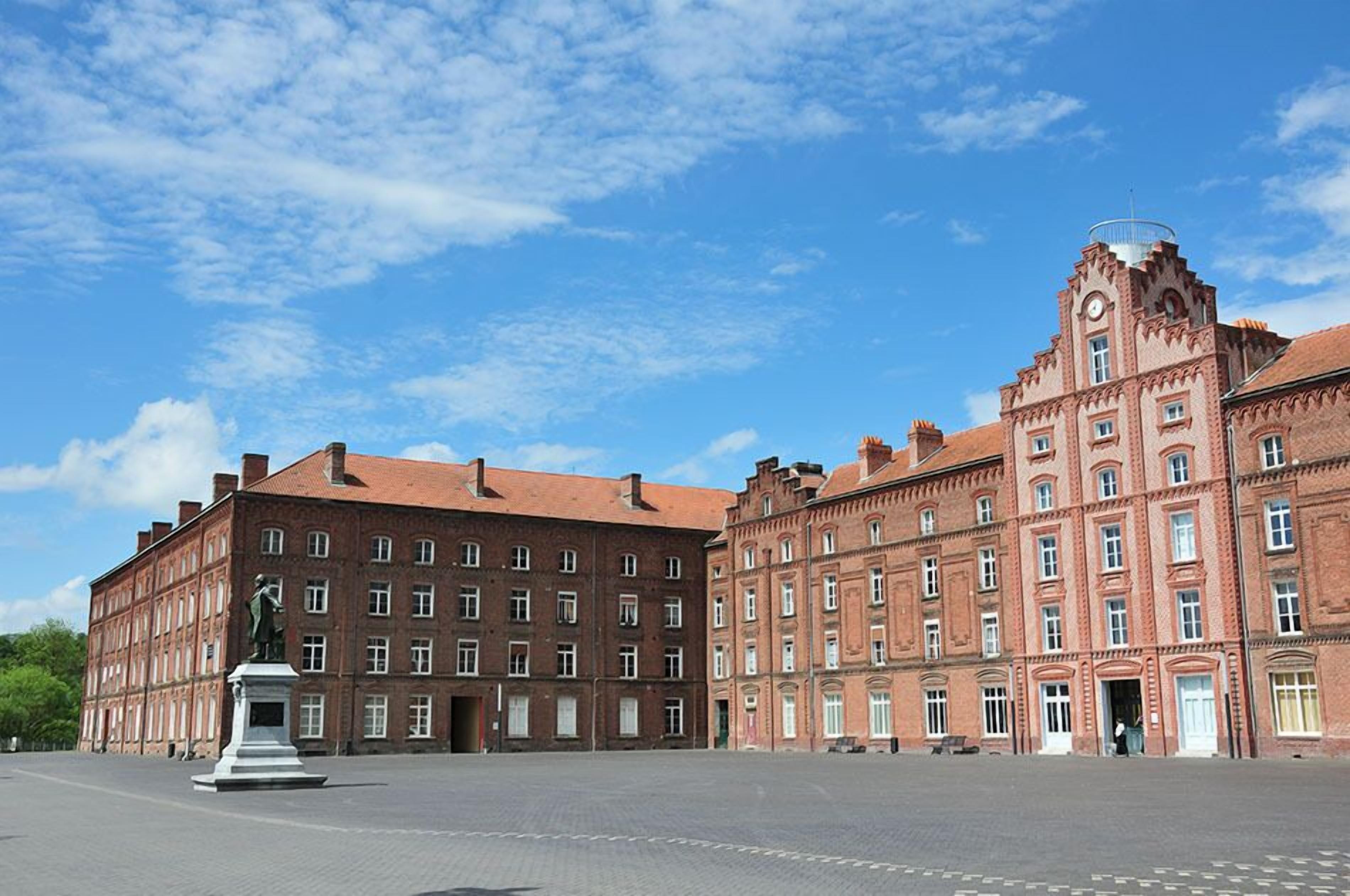 A large, historic building with a central courtyard, featuring a statue and a clock tower.