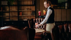 En person som serverar drycker vid ett bord i ett rum med lädermöbler, en bokhylla och en jordglob på väggen.