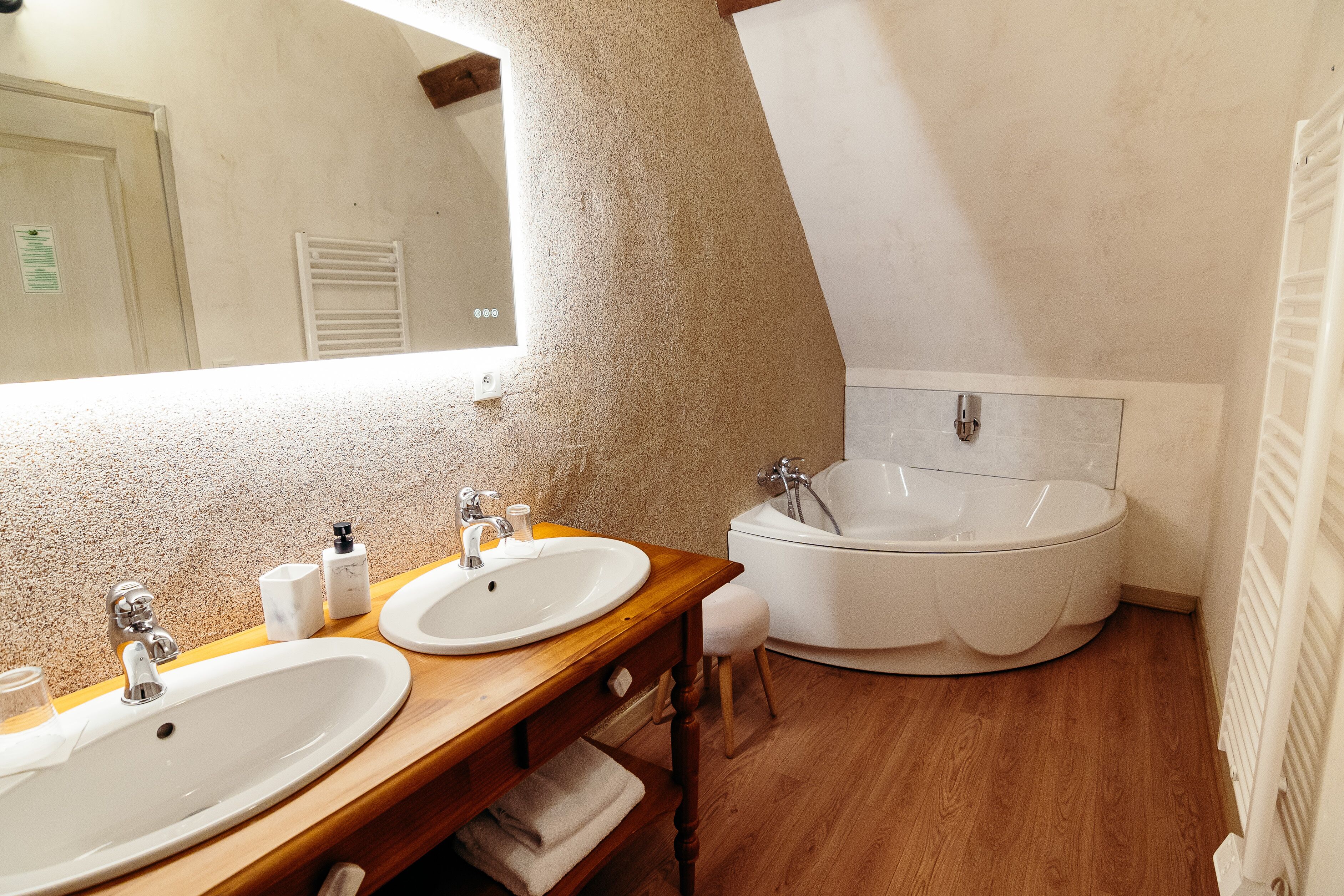 A bathroom with two sinks, a bathtub, wooden vanity, and a large mirror.