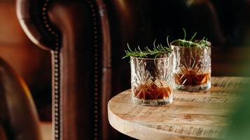 Dos vasos de whisky con romero sobre una mesa de madera en una habitación tenuemente iluminada con un sillón de cuero.