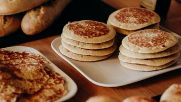 A table with various baked goods, including pancakes, bread, and pastries.