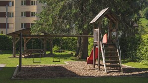 A playground with a slide and swings, surrounded by trees and a building in the background. - Youth Hostel Engelberg (Engelberg)