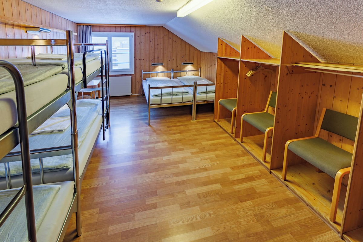 A dormitory room with bunk beds, a desk, and a chair.