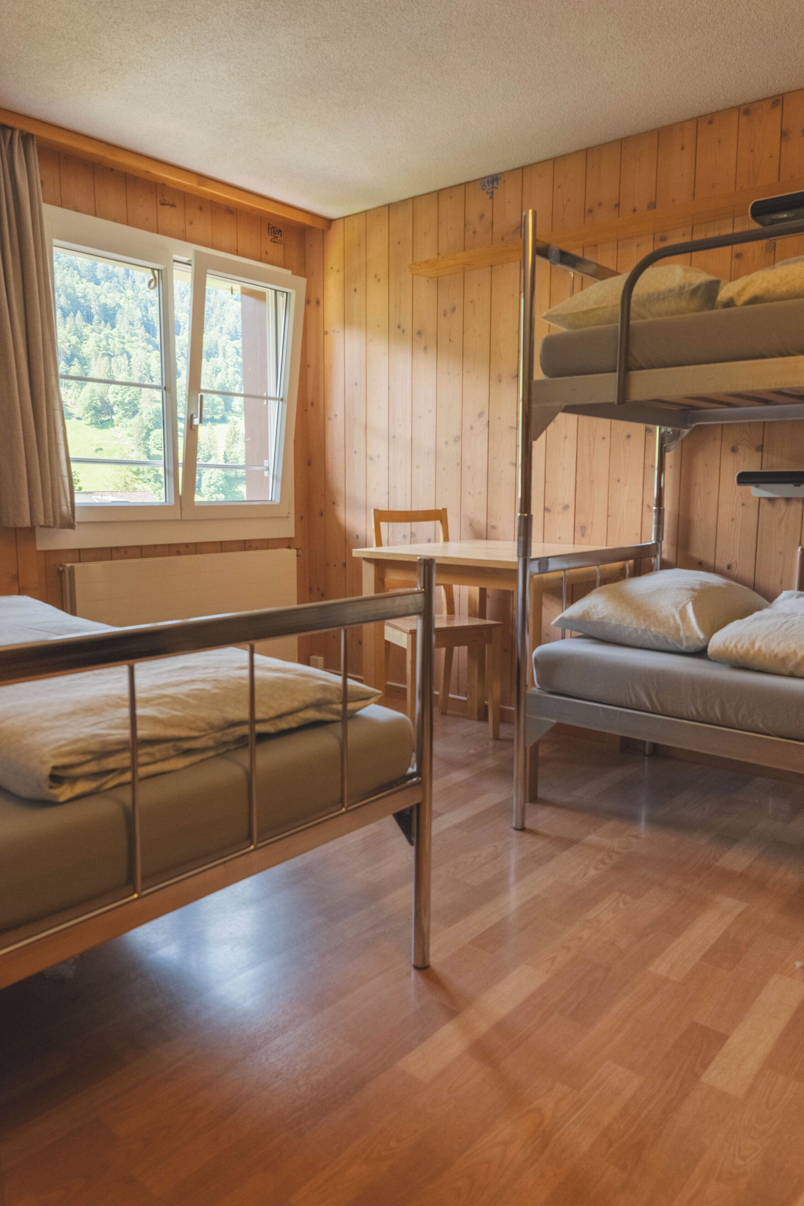 Habitación con literas, paredes de madera, una ventana con cortinas, una mesa y una silla.