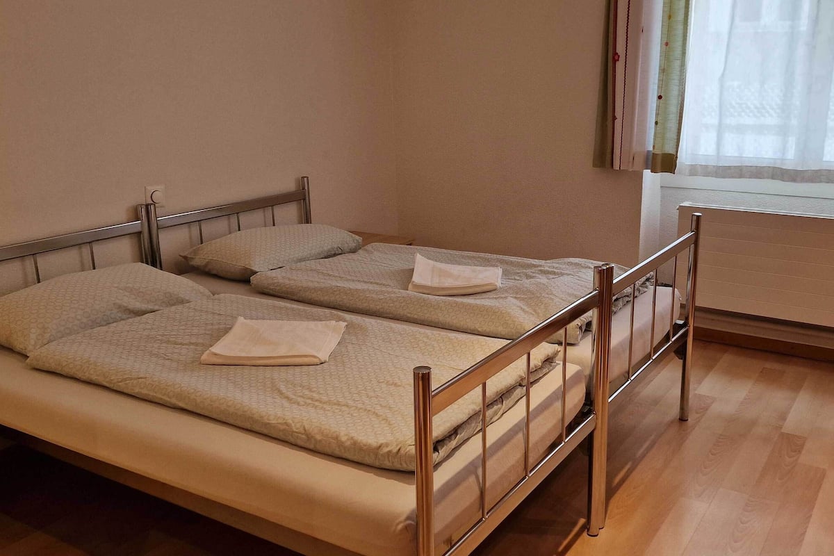 A single bed with a metal frame and a wooden headboard in a room with wooden flooring and a radiator.