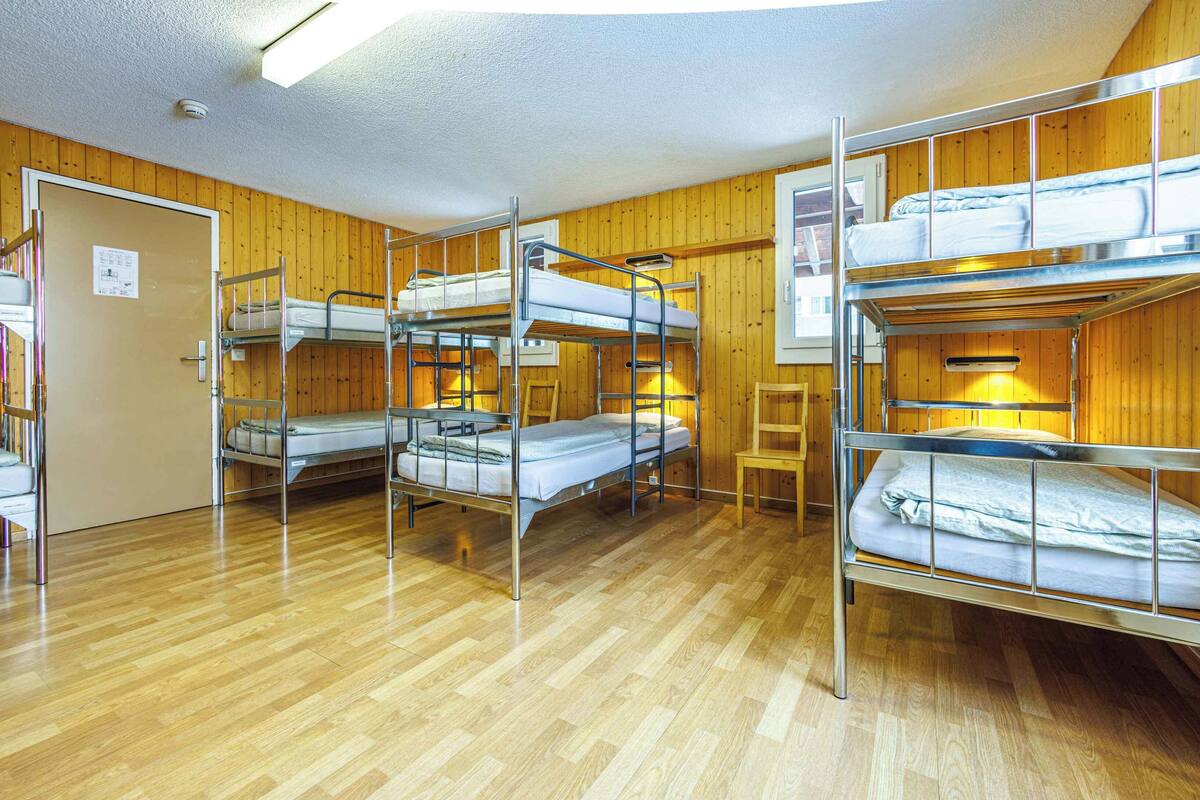 A dormitory room with bunk beds, wooden walls, and a wooden floor.