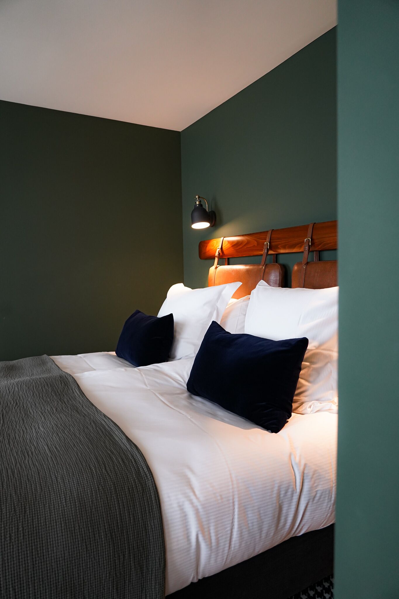 A neatly made bed with white and navy blue pillows, a wooden headboard, and a bedside lamp.