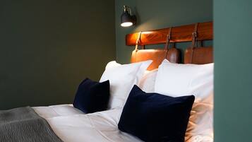 A neatly made bed with white and navy blue pillows, a wooden headboard, and a bedside lamp.