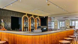 A modern bar area with a wooden counter, bar stools, and shelves of bottles. - Le Tonnelier (Bulle)